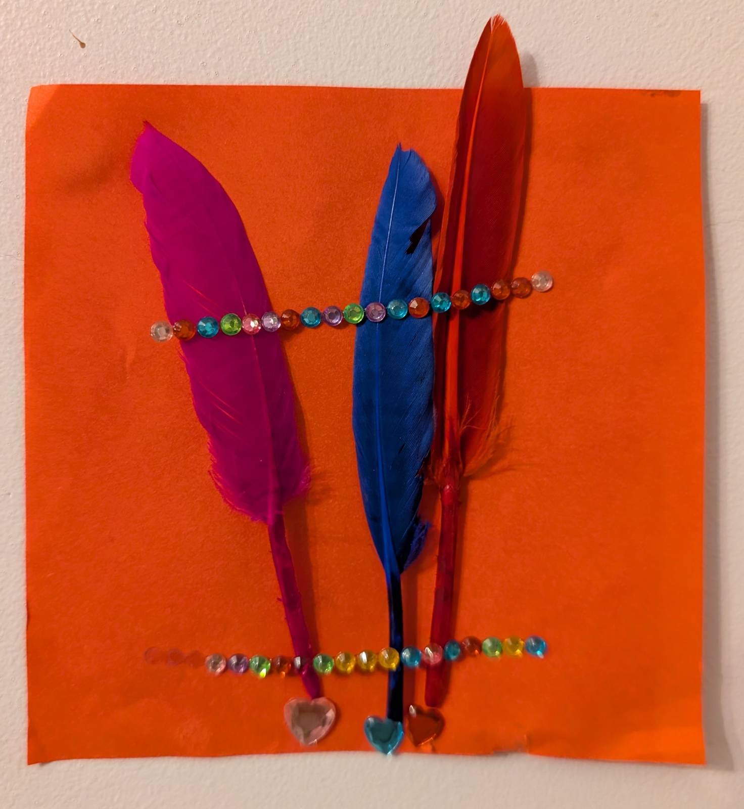 Pink, blue and red feathers decorated with gemstone strips on an orange background